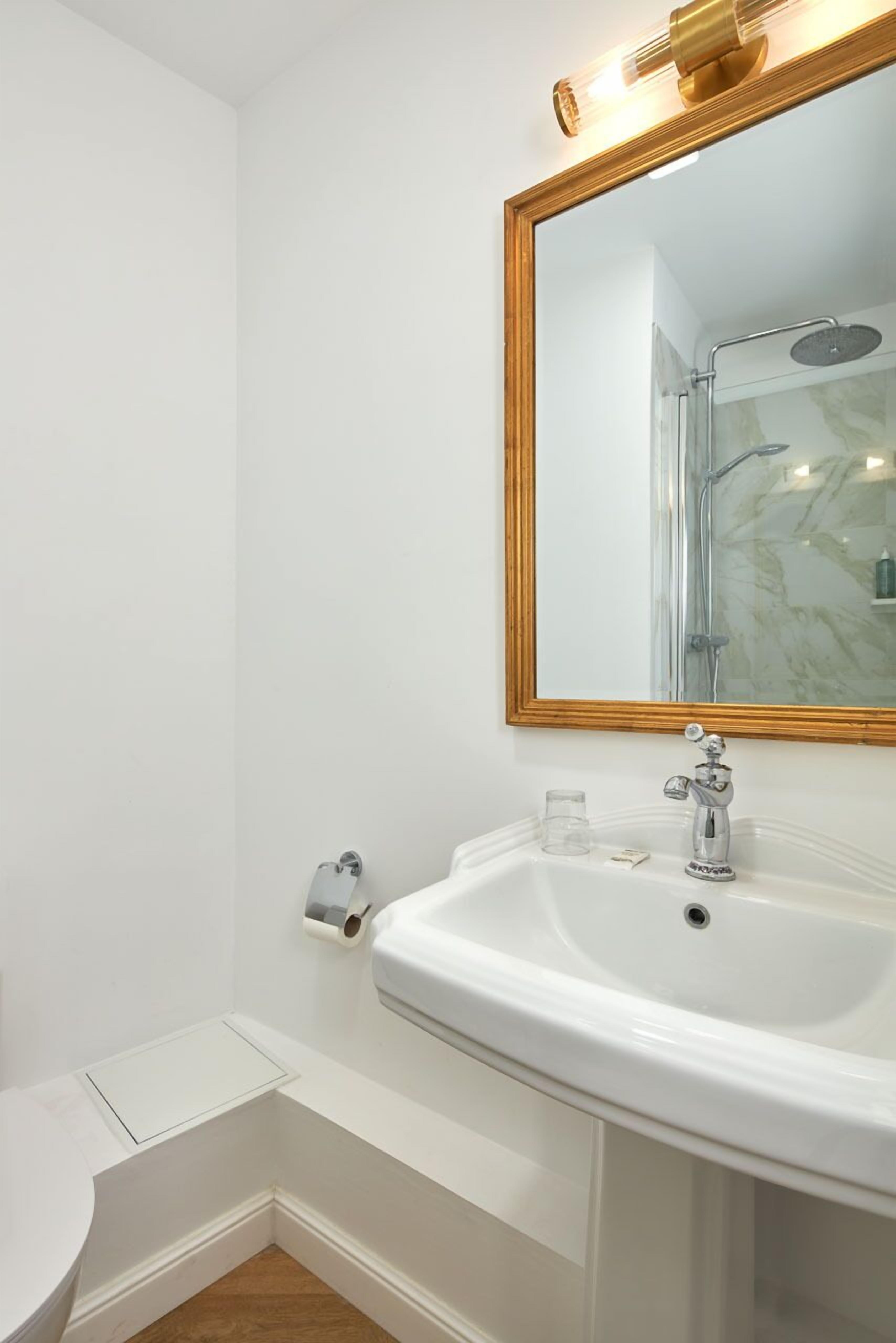 Une salle de bain avec un lavabo blanc, un miroir avec un cadre doré et un espace douche.