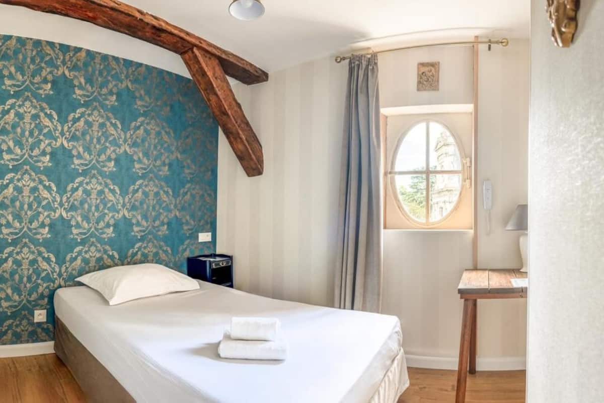 A bedroom with a bed, a wooden headboard, a window with curtains, and a small table with a lamp.