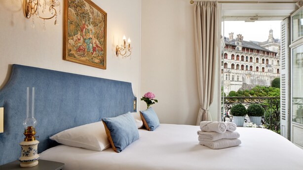 Una habitación de hotel con una cama grande, un candelabro, un cuadro y vistas a un edificio histórico.