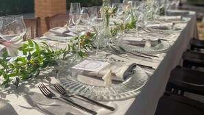Une longue table à manger installée à l’extérieur, agrémentée de beaux verres, d’assiettes et de couverts.
