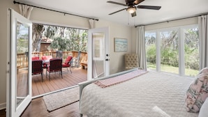 Ein Schlafzimmer mit einem großen Bett, einem Deckenventilator und Blick auf eine Terrasse mit Gartenmöbeln.