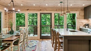 Ein Holzblockbau-Innenraum mit Essbereich, Küche und großen Fenstern mit Blick auf den Wald.