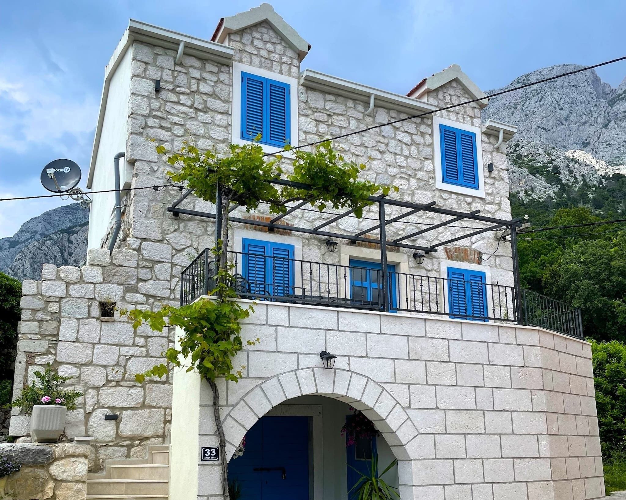 A stone building with blue shutters, a satellite dish, and a sign indicating the address.