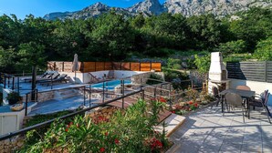 Une terrasse sur le toit dotée d’une piscine, d’un espace salon extérieur et d’un coin barbecue, le tout entouré d’une végétation luxuriante et de montagnes.