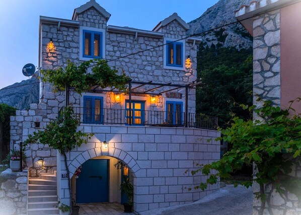 A stone building with a blue door and shutters, a small staircase leading to the entrance, and a view of the surrounding landscape. - Villa Didovina with pool (Tucepi)