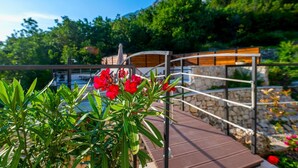 Une terrasse en bois avec une balustrade en pierre, donnant sur une étendue d’eau et une végétation luxuriante.