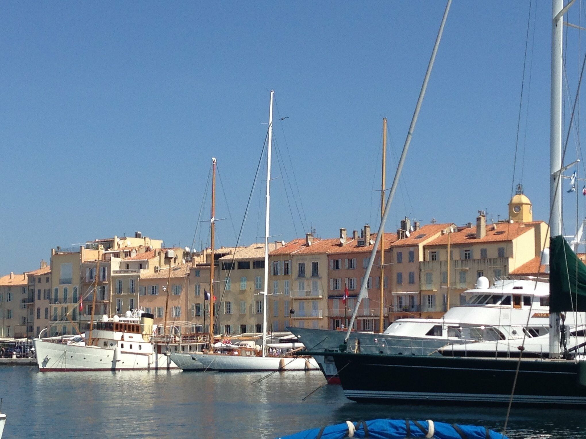 Un port de plaisance avec des bateaux amarrés, des bâtiments en arrière-plan et un ciel dégagé.