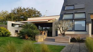 Et moderne hus med en overdækket terrasse, en stensti og en velplejet græsplæne.