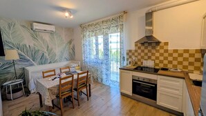 Cocina compacta con comedor, que cuenta con un respuesto a cuadros, estufa y ventana con cortinas.