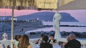 Un comedor con mesas y sillas, una estatua y vistas a la playa y el océano.