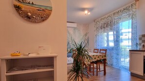 Un área de comedor con una mesa, sillas, una planta en maceta e imagen colgada en la pared.