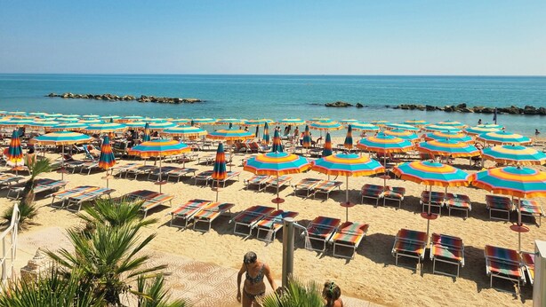 Una playa con numerosos sombrillas de colores y tumbonas.