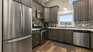 A modern kitchen with stainless steel appliances, dark wood cabinets, and a large window providing natural light. - Luxury Living – Walk to Poudre Trail and Old Town! (Fort Collins)