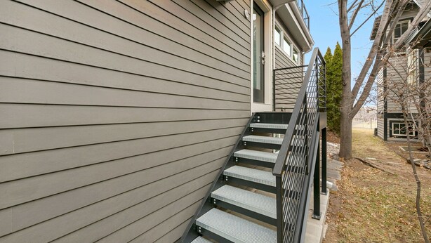A residential building with a grey siding exterior, a metal staircase with a handrail, and a small tree in the foreground. - Luxury Living – Walk to Poudre Trail and Old Town! (Fort Collins)