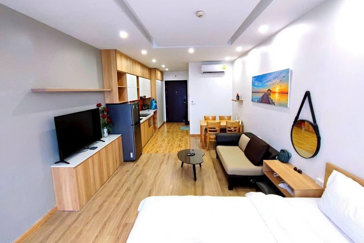 A compact hotel room with a bed, a TV, a small kitchenette, a dining area, and a bathroom.