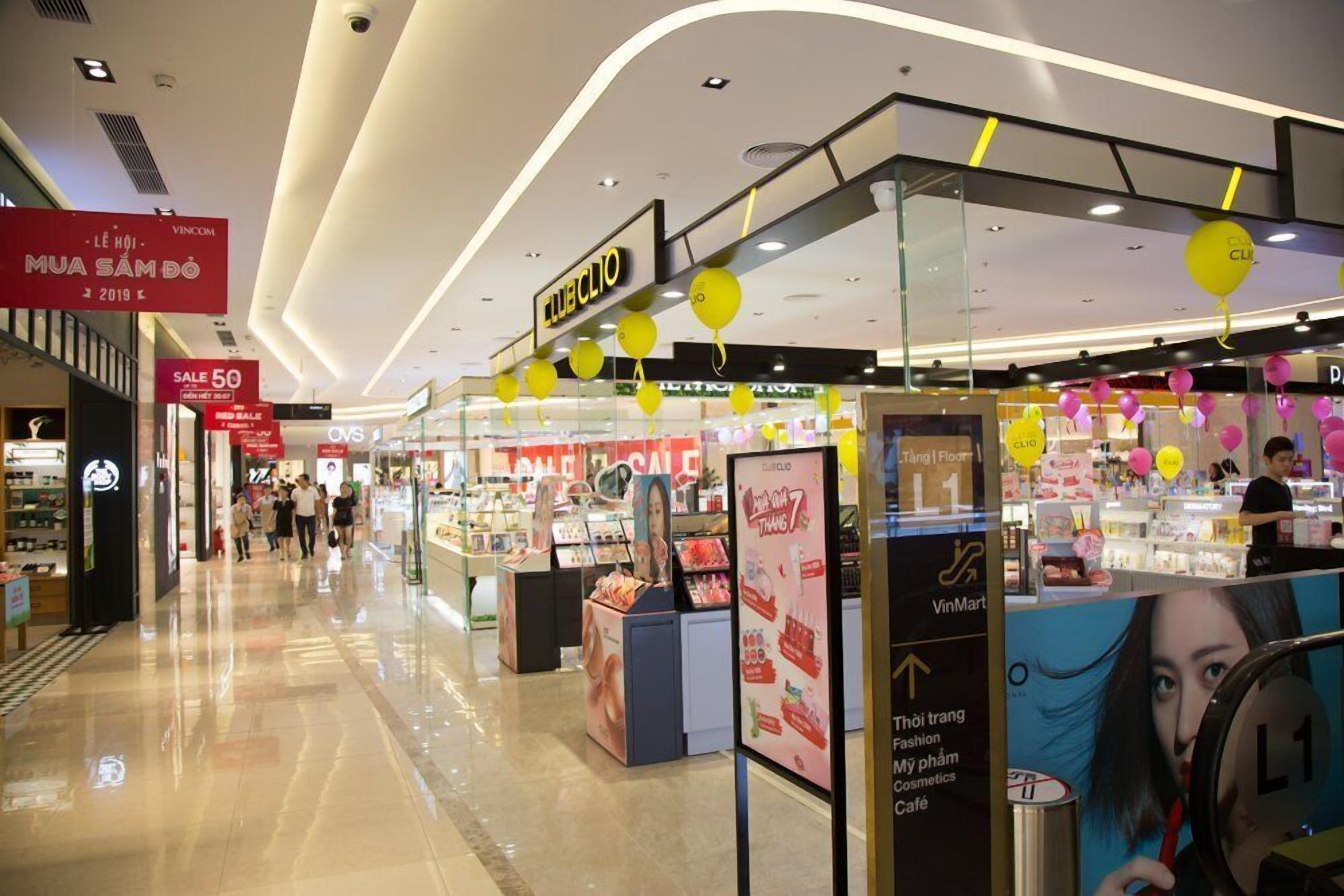 Un pasillo de centro comercial con una tienda ClubClio, adornado con globos amarillos y letreros promocionales.