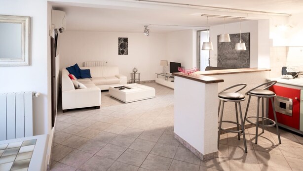 Una sala de estar moderna con un sofá blanco, una mesa de centro y una cocina con encimera roja y taburetes de bar.