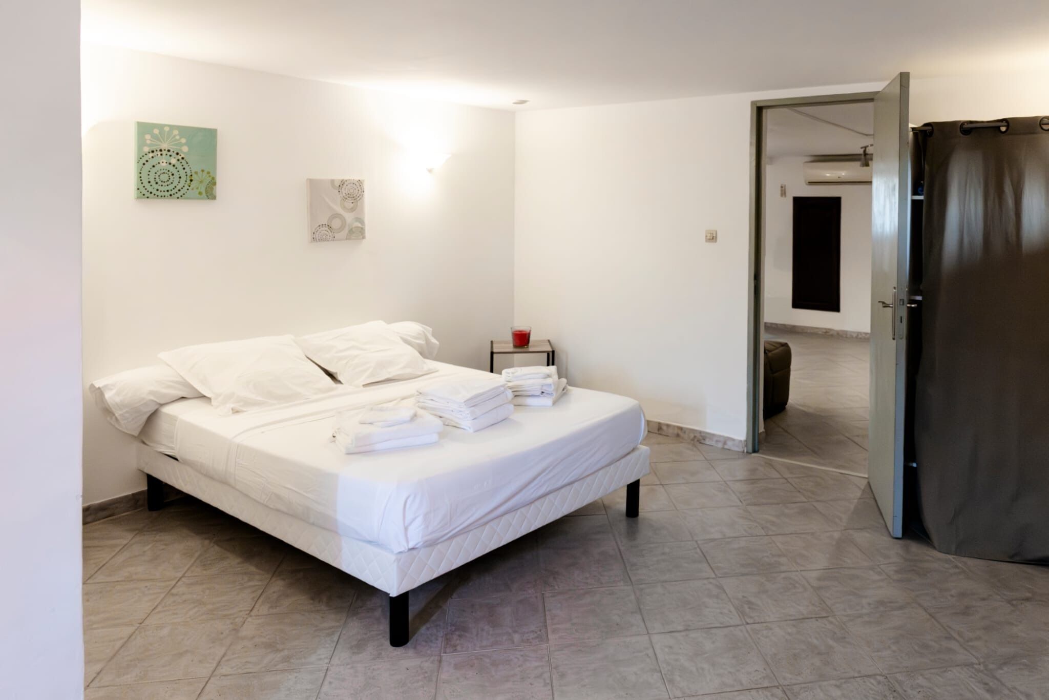 A neatly made bed with white linens and towels, a bedside table with a red cup, and a door leading to another room.