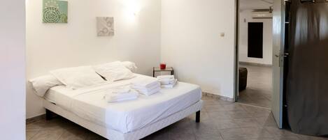 A neatly made bed with white linens and towels, a bedside table with a red cup, and a door leading to another room.