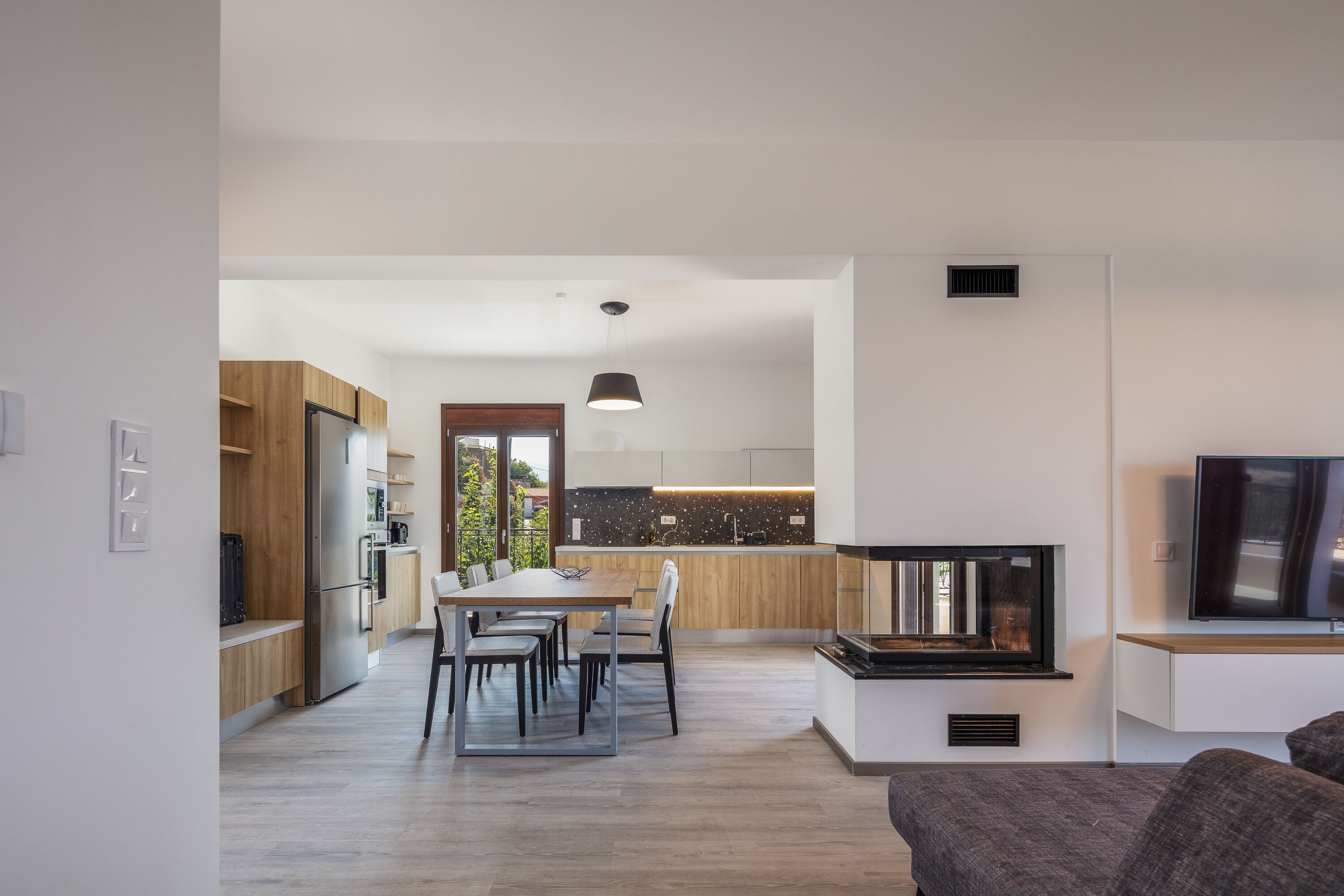 A modern kitchen with wooden cabinets, a dining area with a table and chairs, and a built-in TV.