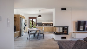 A modern kitchen with wooden cabinets, a dining area with a table and chairs, and a built-in TV. - Suites Olive Tree Farm Episkopi Village (Rethymno)
