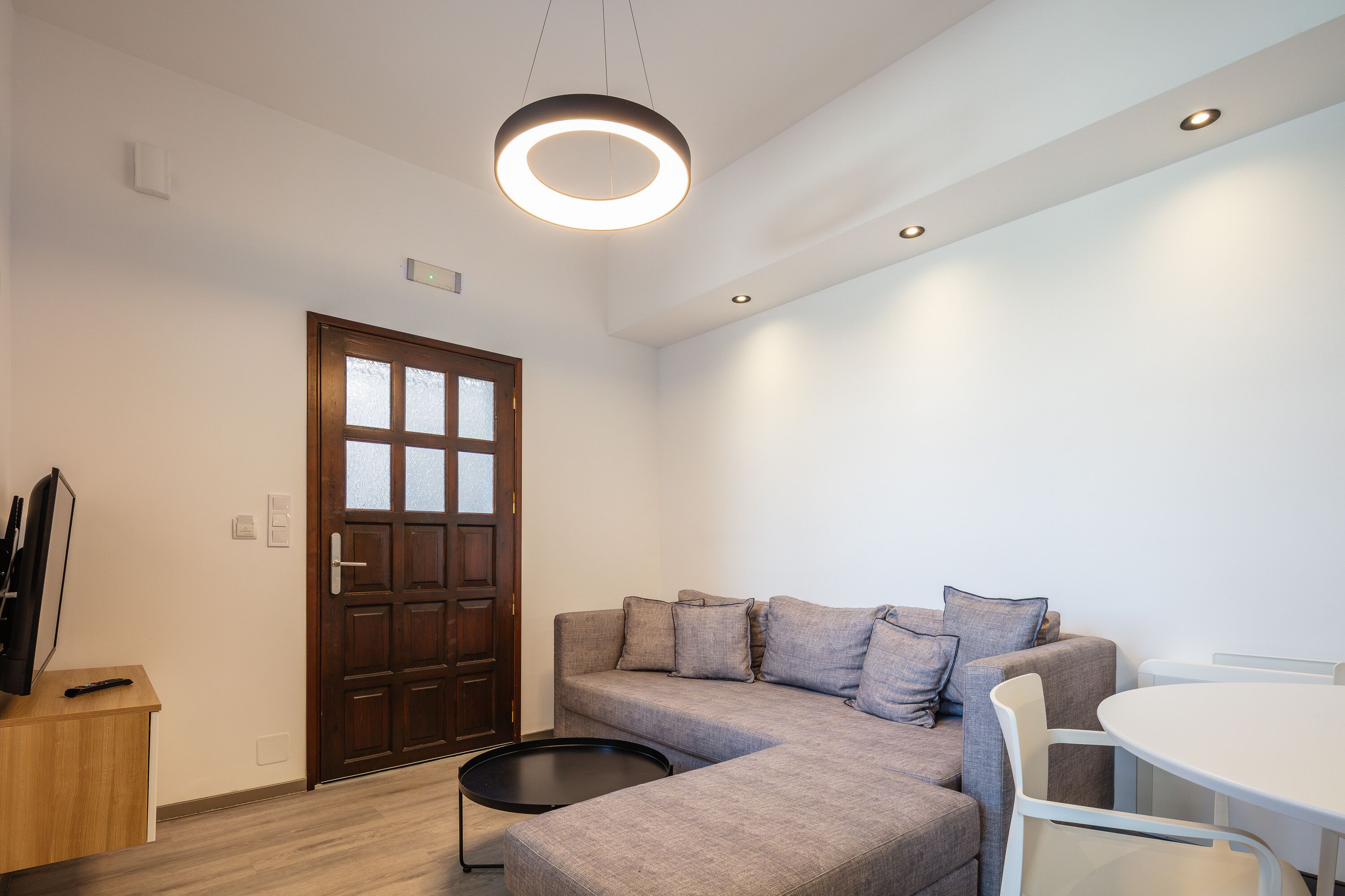 Un salon moderne avec un canapé d’angle, une table basse ronde et un coin repas comprenant une table et des chaises blanches.