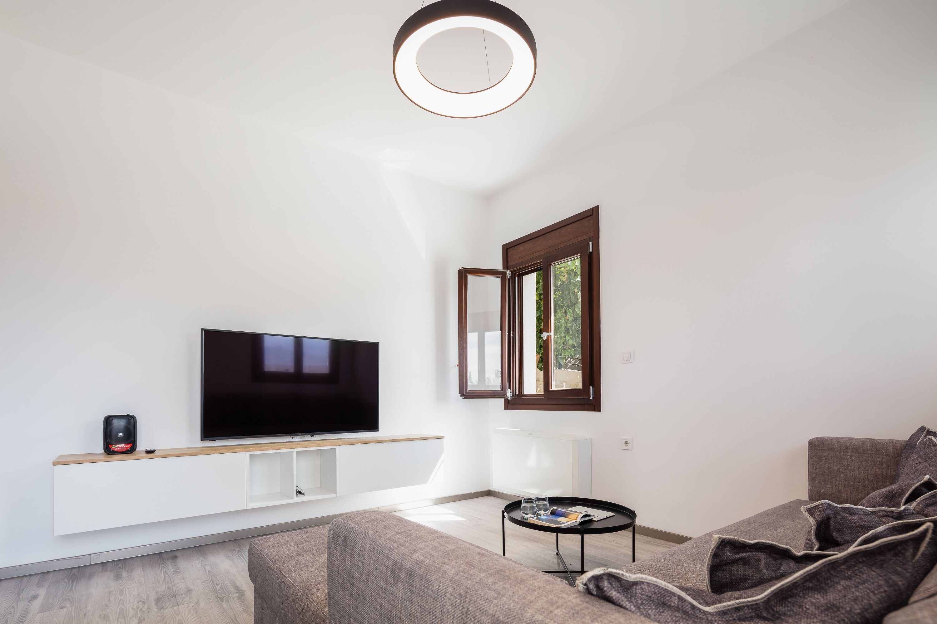 A modern living room with a flat-screen TV, a coffee machine, and a small table with a magazine.