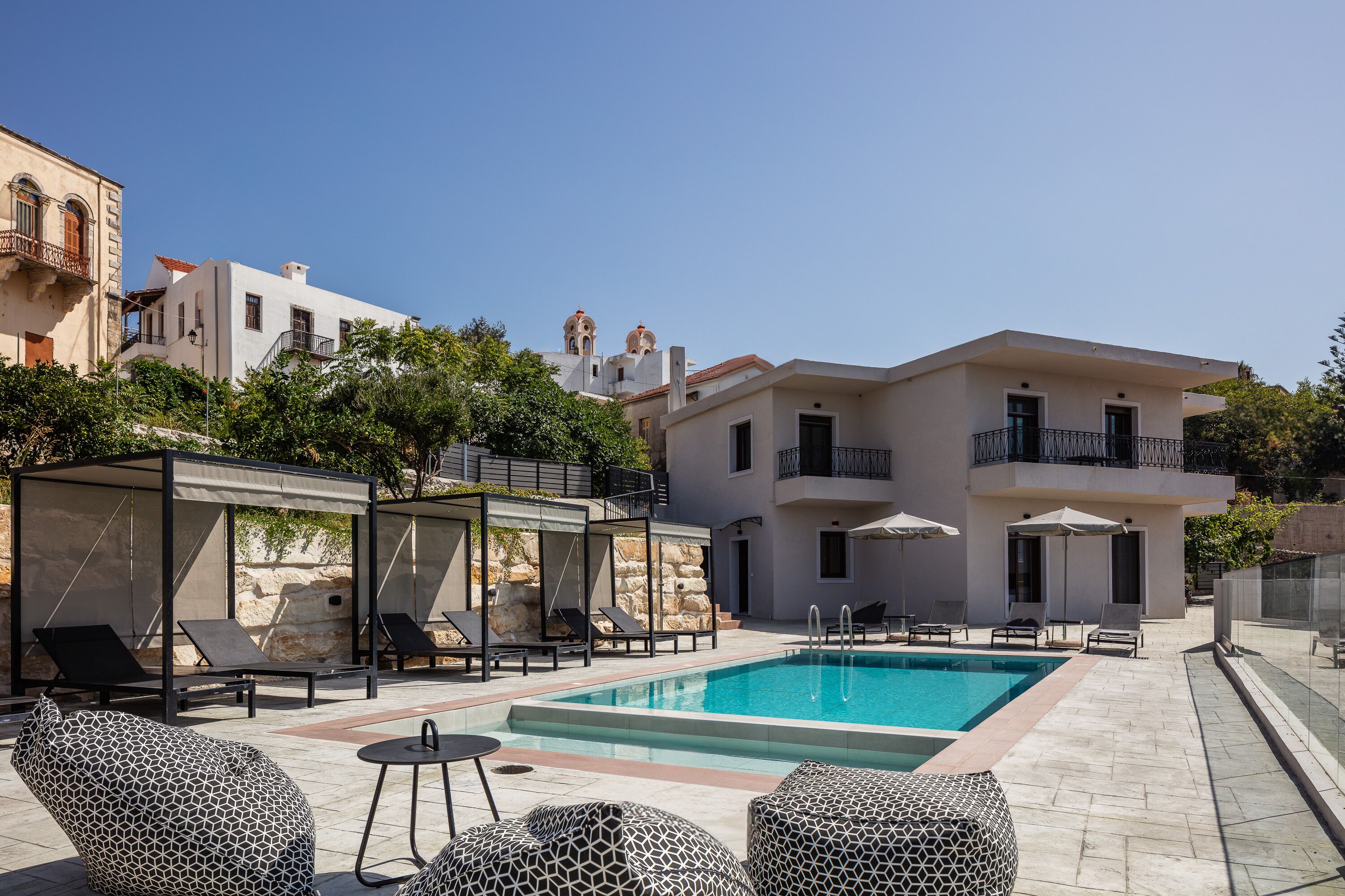 Uma área de piscina com espreguiçadeiras, um espaço de estar coberto e um edifício com varandas e piscina.