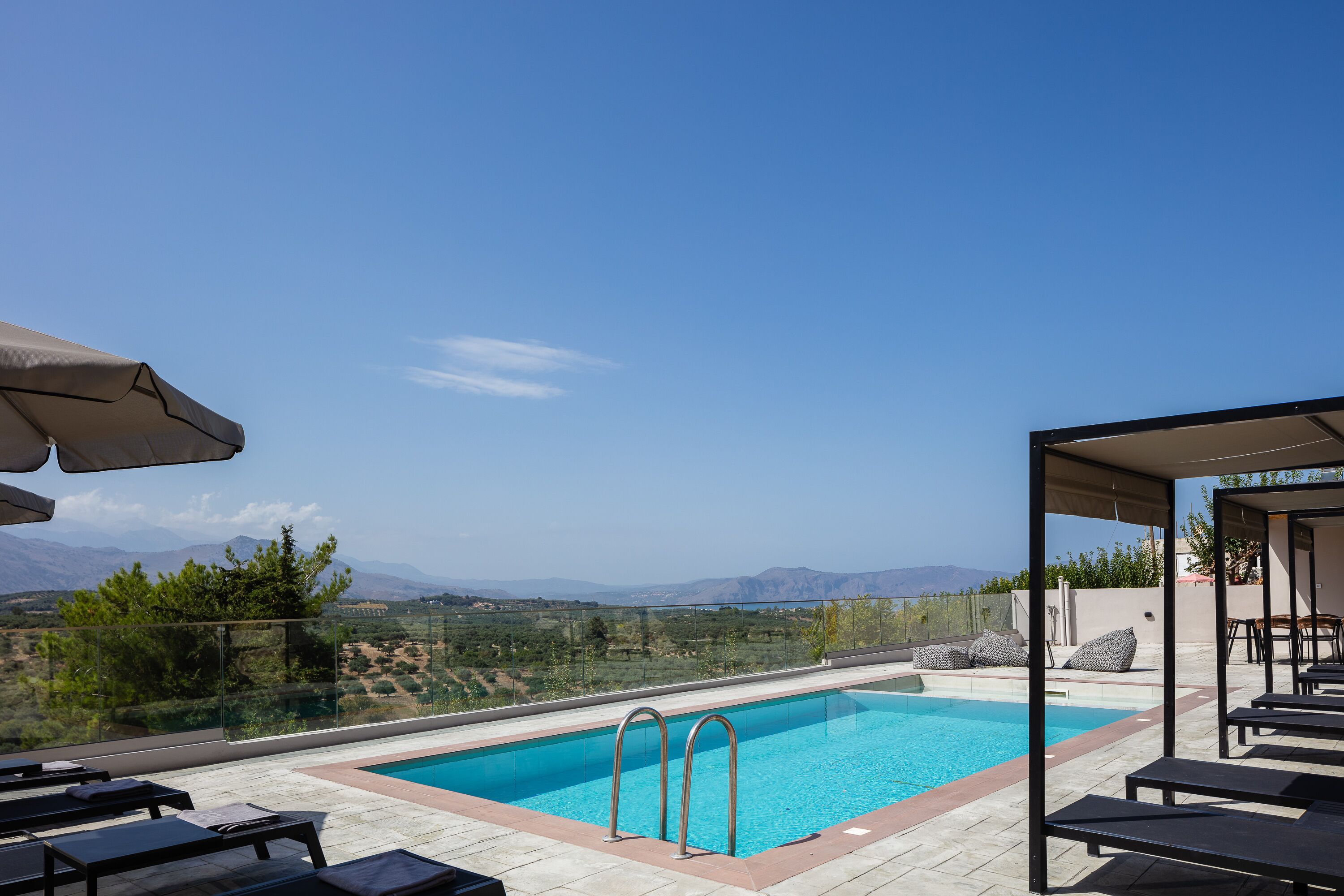 Une piscine sur le toit, avec une eau d’un bleu cristallin, entourée de chaises longues et bordée d’une rambarde en verre, offrant une vue panoramique sur un paysage magnifique, avec des montagnes et une végétation luxuriante.