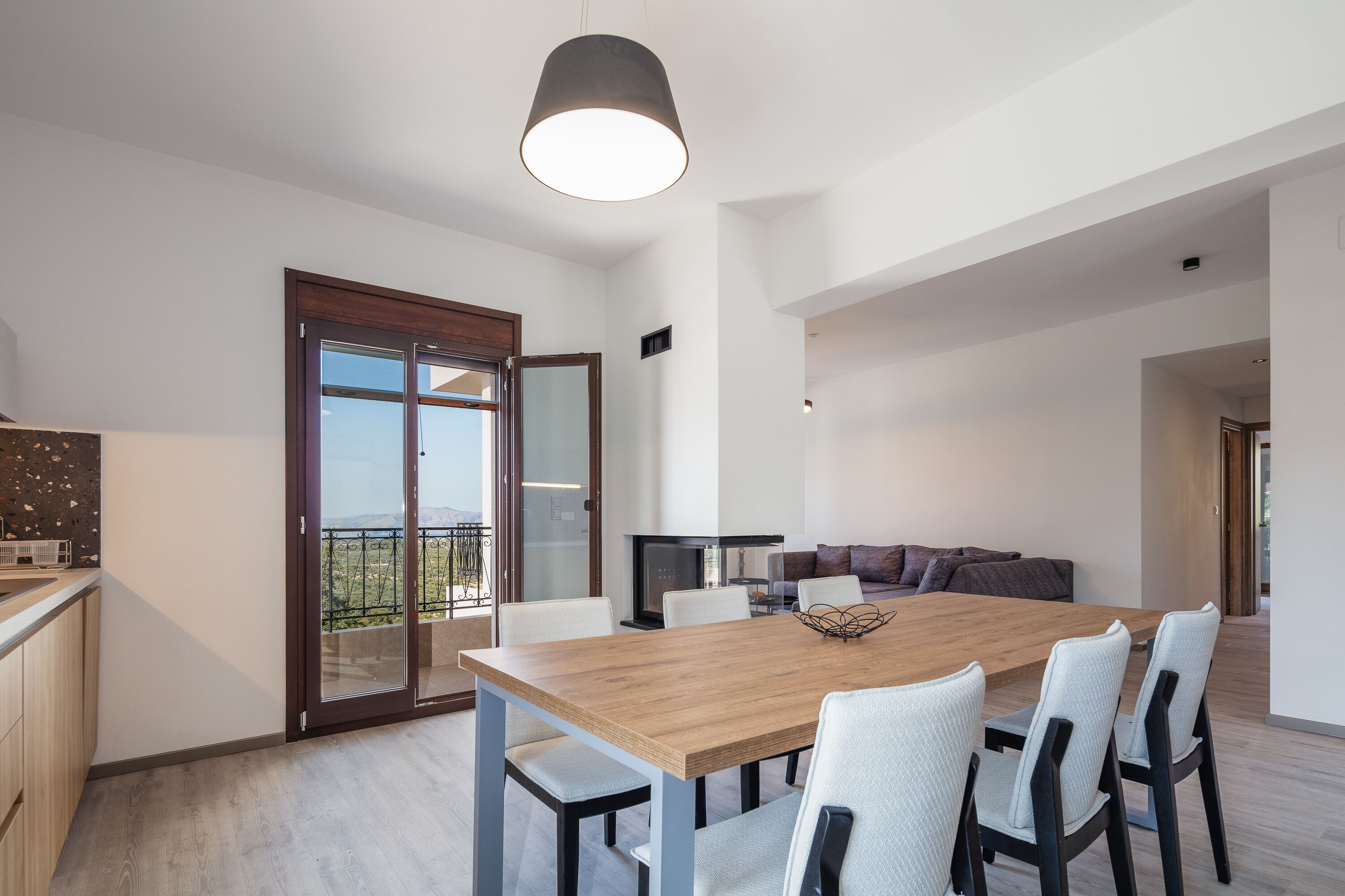 A modern kitchen with a wooden countertop, a dining area with a wooden table and chairs, and a living area with a sofa and a TV.