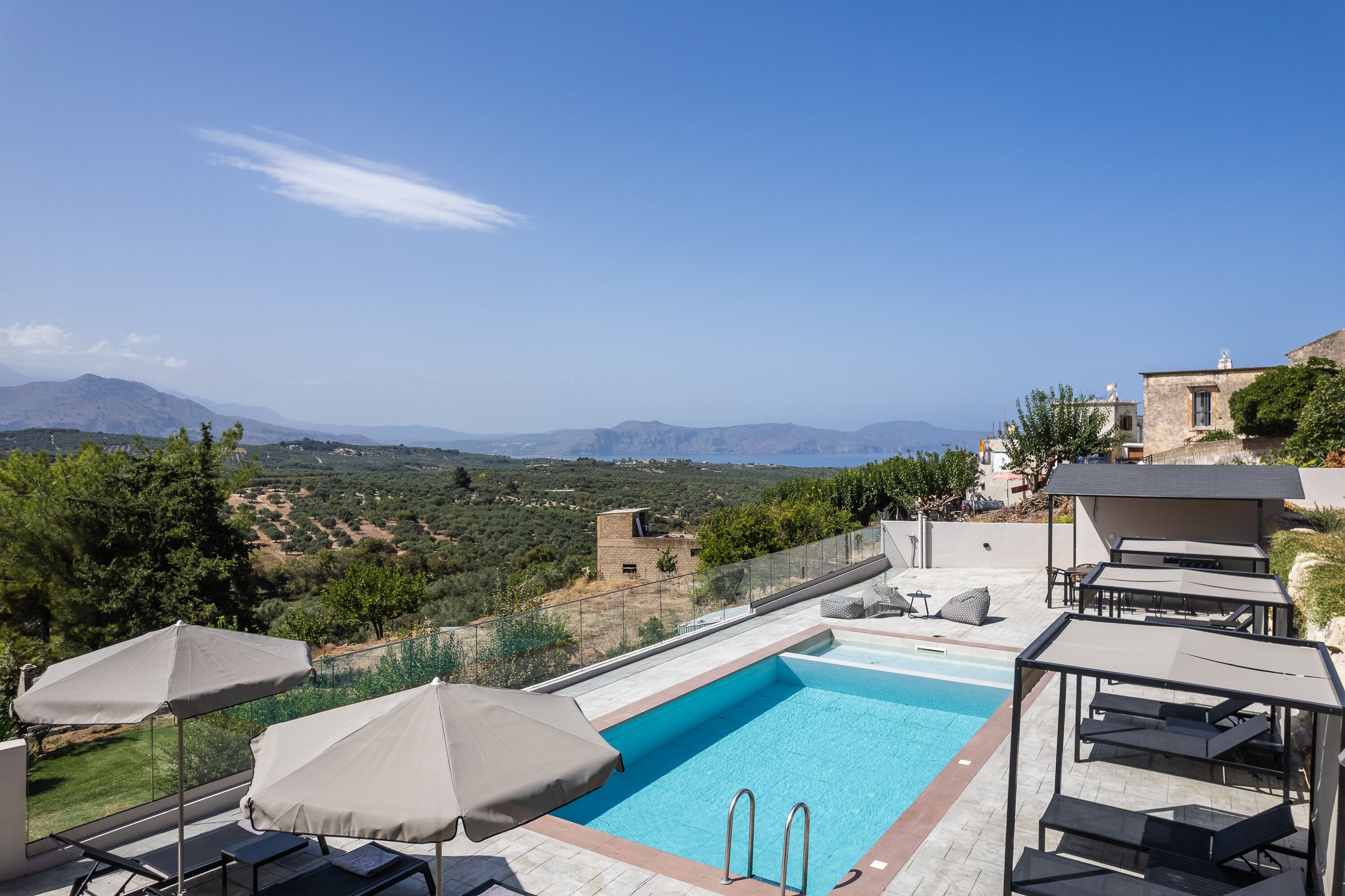 A rooftop pool with clear blue water, surrounded by lounge chairs and umbrellas, overlooking a scenic landscape with mountains and greenery.