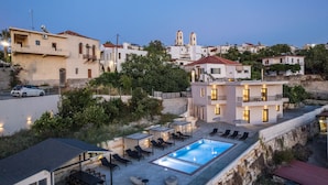 A rooftop pool area with lounge chairs, a swimming pool, and a view of the surrounding hillside buildings. - Suites Olive Tree Farm Episkopi Village (Rethymno)