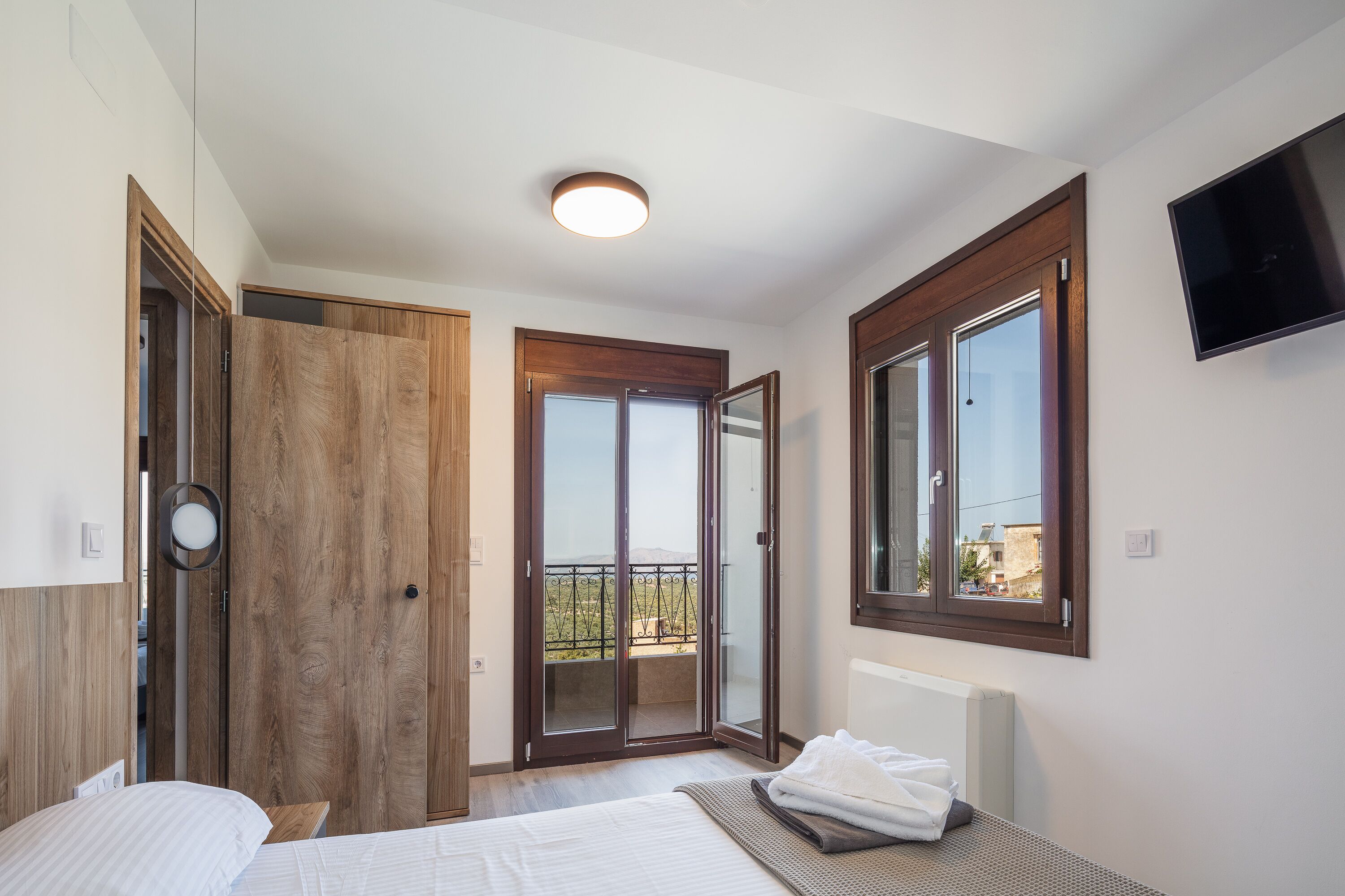 Un dormitorio con cama, mesita de noche, televisor, ventana y puerta al balcón.