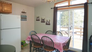 Zona pranzo con tavolo apparecchiato per quattro persone, circondato da sedie, un lampadario e vista attraverso un'ampia finestra.