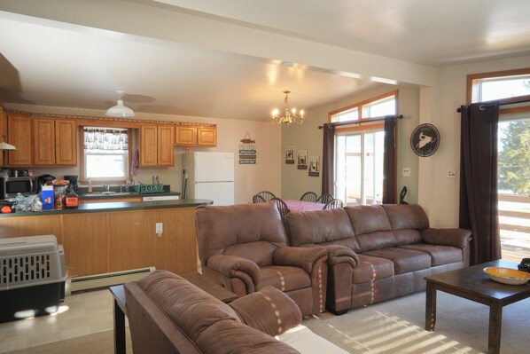A spacious living room with a brown leather sofa and a dining area with a table and chairs.