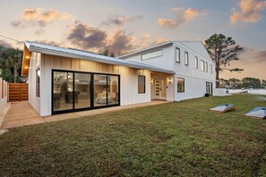 A modern two-story house with a large glass sliding door entrance, a covered patio, and a well-maintained lawn. - Gorgeous Waterfront Luxury Beach House Sleeps 22, Pool, Kayaks (Panama City Beach)