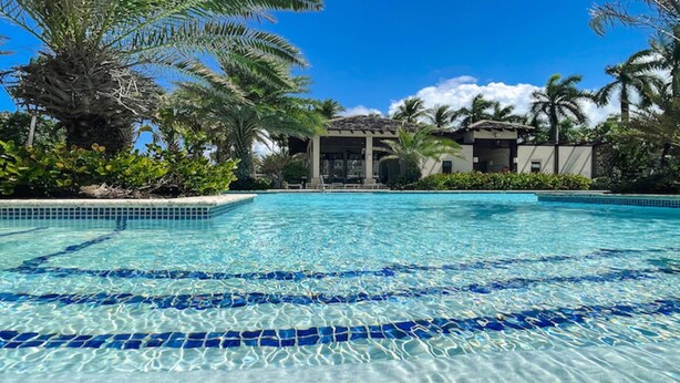 Una piscina cristalina con azulejos azules, rodeada de palmeras y un edificio con tejado de cerámica.