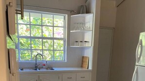 A kitchen with white cabinets, a sink, and a window with a view of greenery. - 2 bedroom house  (Vieux-fort)
