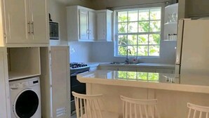 A kitchen with white cabinets, a built-in washing machine, a large window, and a bar area with stools. - 2 bedroom house  (Vieux-fort)