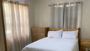 A bedroom with a bed, wooden headboard, curtains, and an air conditioning unit. - 2 bedroom house  (Vieux-fort)
