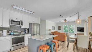 Una cucina moderna con mobili bianchi, elettrodomestici in acciaio inossidabile e un'isola centrale con sgabelli.