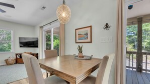 Un'area pranzo con tavolo in legno, sedie imbottite color beige, lampadario a sospensione e un quadro appeso al muro.