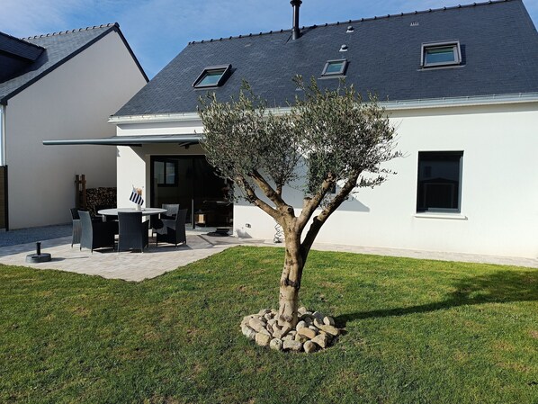 Ein modernes Haus mit gepflegtem Rasen, einer Terrasse mit Gartenmöbeln und einem Baum in der Mitte.