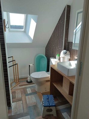 Ein kleines Badezimmer mit Oberlicht, Toilette, Waschbecken und einer kleinen Bank.
