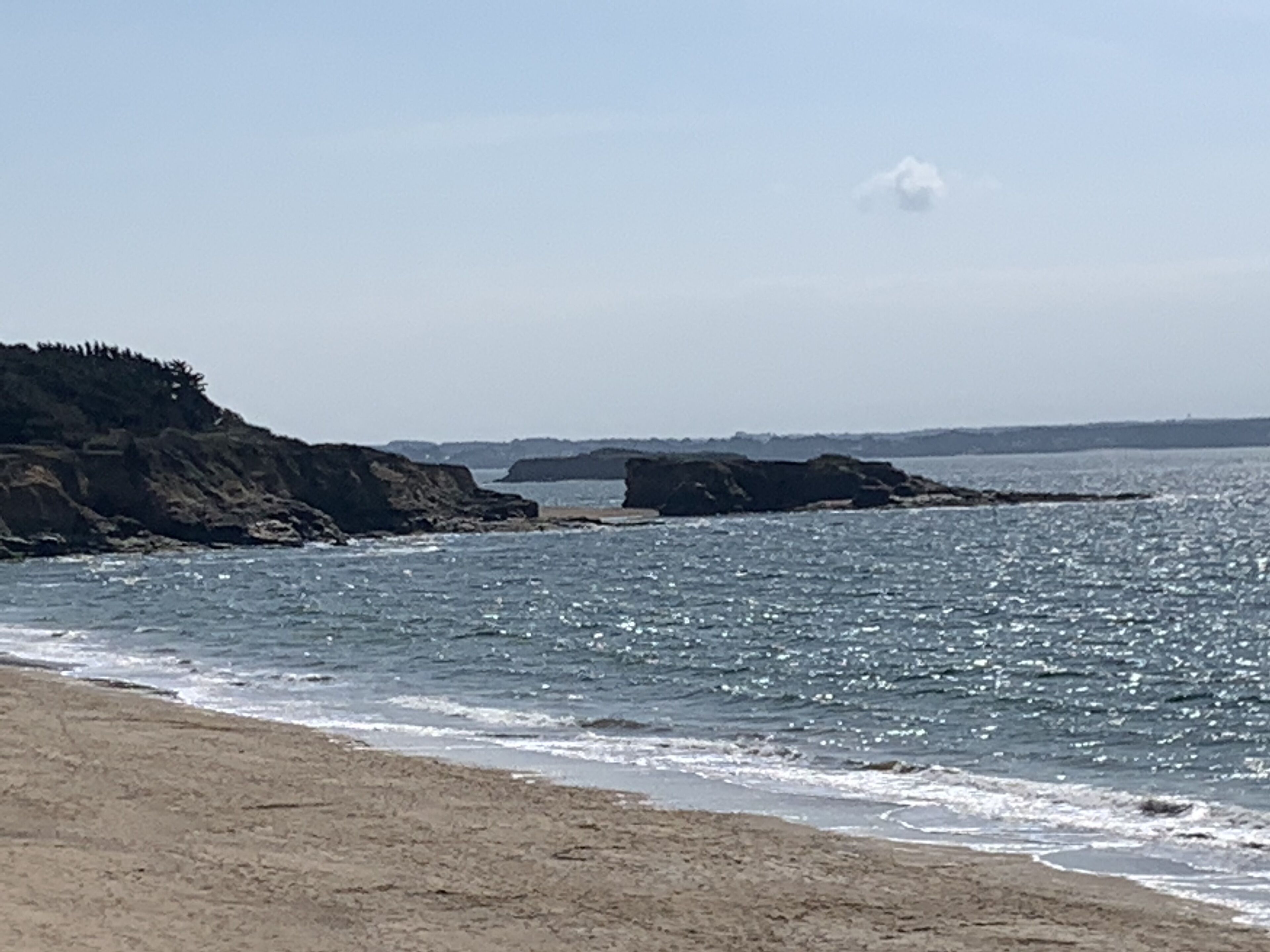 Une plage avec des affleurements rocheux et des vagues douces.