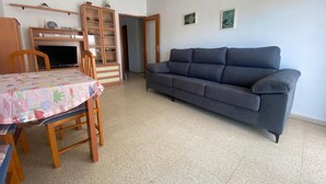 A living room with a sofa, a dining table with chairs, a television, and a cabinet.