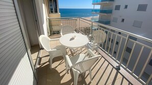 A balcony with a table and chairs, overlooking a beach and a building with multiple balconies.