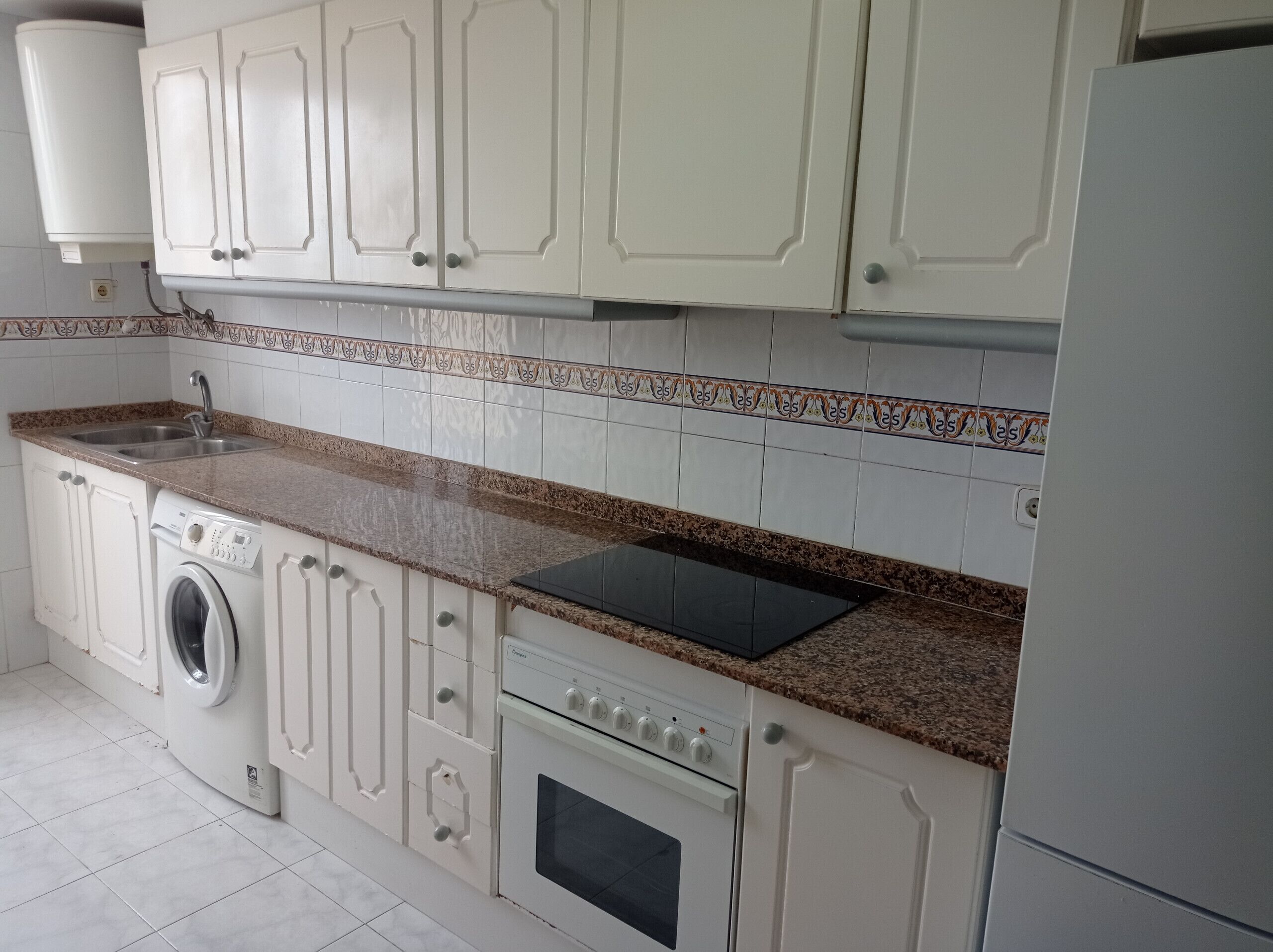 A kitchen with white cabinets, a washing machine, a stove, and a sink.