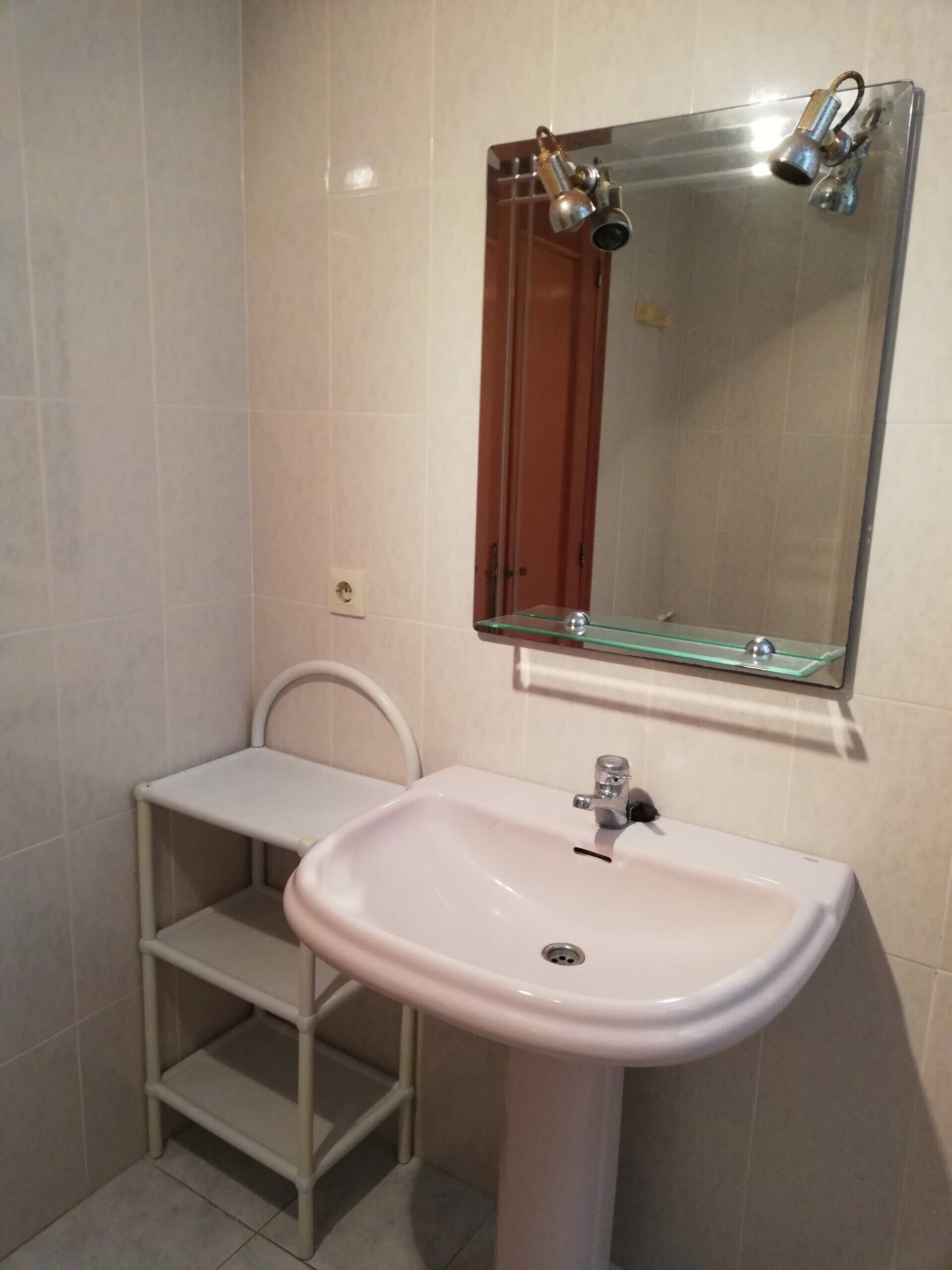 A bathroom with a white pedestal sink, a glass shelf, and a mirror with a shower head above it.
