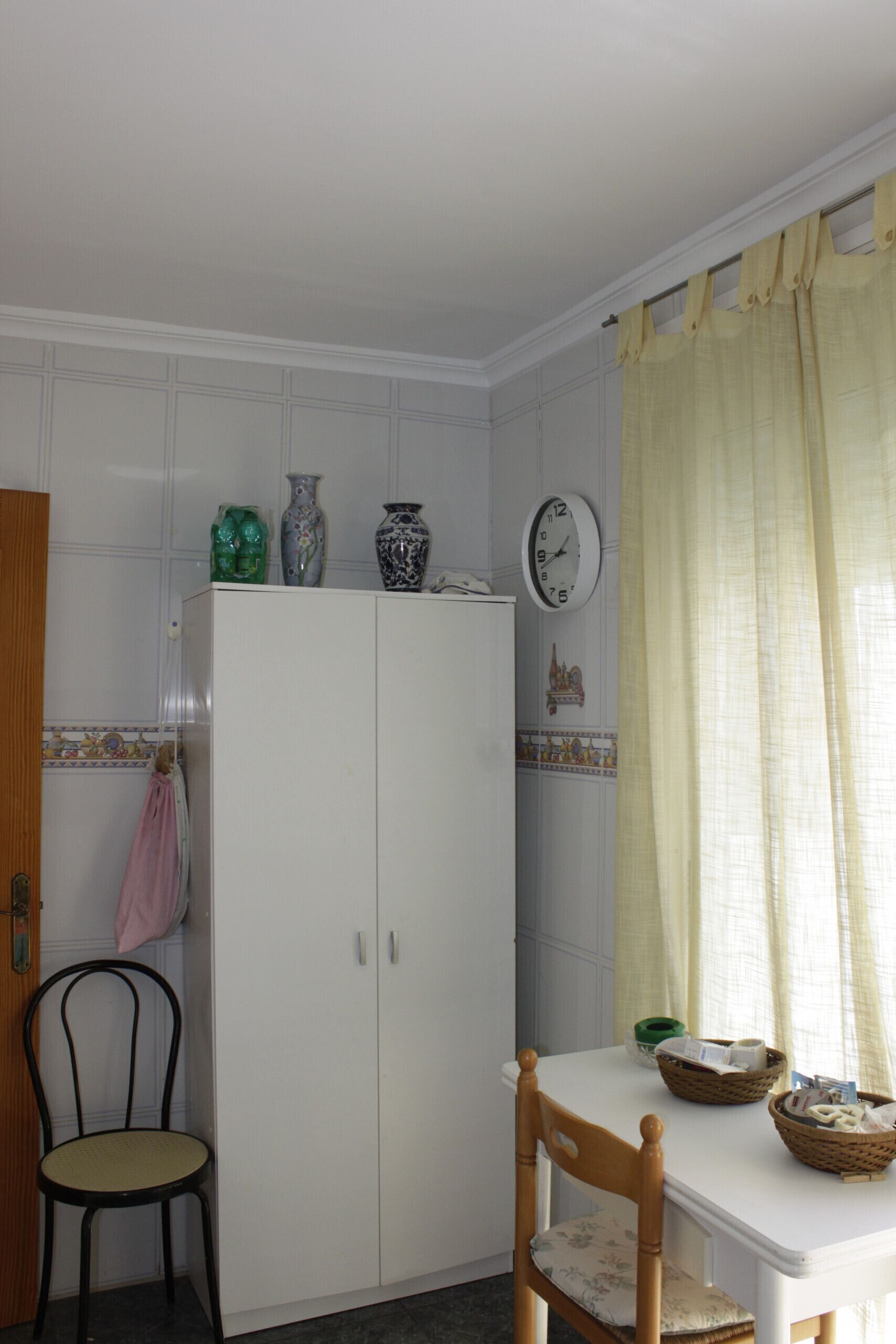Ein Zimmer mit einem weißen Kleiderschrank, einem Esstisch mit Stühlen und einem Fenster mit Vorhängen.